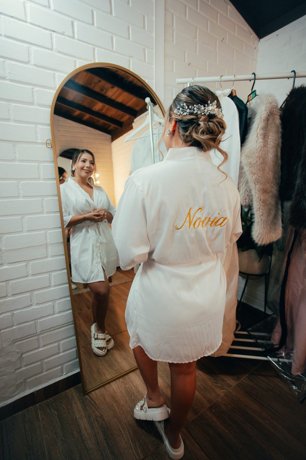 La novia frente al espejo de arco junto al rack de vestidos